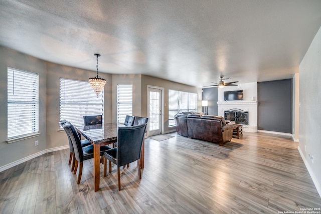 dining room with ceiling fan with notable chandelier, light hardwood / wood-style flooring, and a textured ceiling