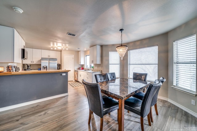 dining space featuring an inviting chandelier, sink, a textured ceiling, and hardwood / wood-style flooring