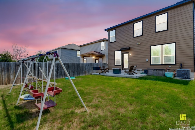 back house at dusk with a playground, cooling unit, a lawn, and a patio area