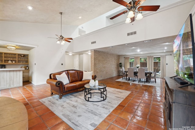 tiled living room featuring ceiling fan, brick wall, and high vaulted ceiling