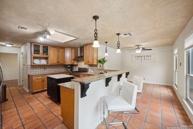 kitchen featuring wall chimney exhaust hood, a breakfast bar area, kitchen peninsula, decorative backsplash, and stove