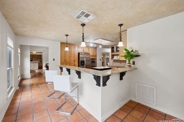 kitchen with backsplash, a kitchen bar, hanging light fixtures, kitchen peninsula, and stainless steel appliances