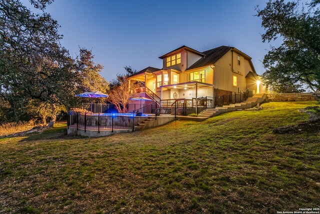 back house at dusk with a fenced in pool, a lawn, and a balcony