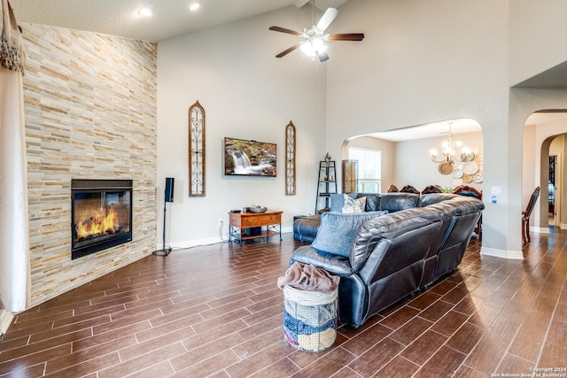 living room with a tiled fireplace, ceiling fan with notable chandelier, and a high ceiling