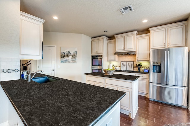 kitchen with a kitchen island, appliances with stainless steel finishes, dark hardwood / wood-style floors, sink, and dark stone counters