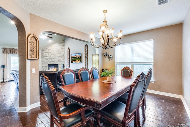 dining space featuring a fireplace, a textured ceiling, dark hardwood / wood-style flooring, ceiling fan with notable chandelier, and vaulted ceiling