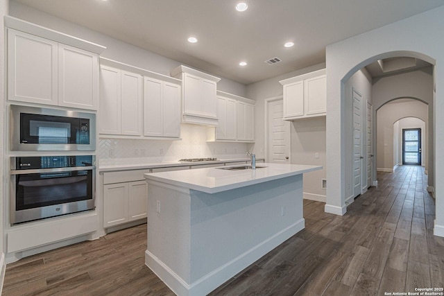 kitchen with an island with sink, white cabinetry, sink, stainless steel appliances, and dark wood-type flooring