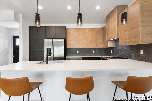 kitchen with hanging light fixtures, stainless steel refrigerator with ice dispenser, sink, and backsplash