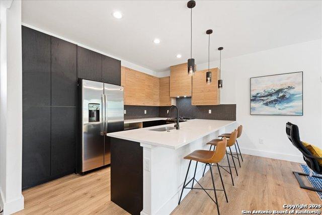 kitchen with pendant lighting, sink, backsplash, a kitchen breakfast bar, and stainless steel refrigerator with ice dispenser