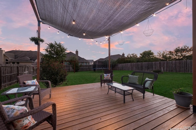 deck at dusk featuring a trampoline and a yard