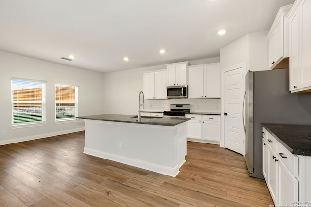 kitchen with stainless steel appliances, a kitchen island with sink, sink, and white cabinets