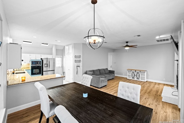 dining room with ceiling fan with notable chandelier and light hardwood / wood-style floors