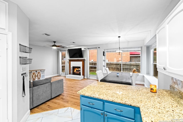 kitchen featuring hanging light fixtures, light stone counters, ceiling fan, light hardwood / wood-style floors, and blue cabinetry