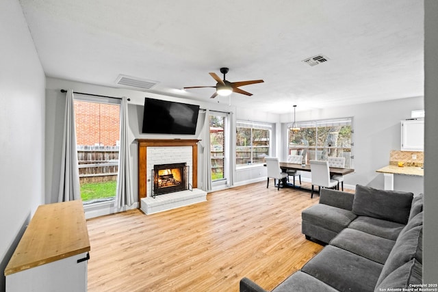 living room featuring ceiling fan, a brick fireplace, and light hardwood / wood-style flooring