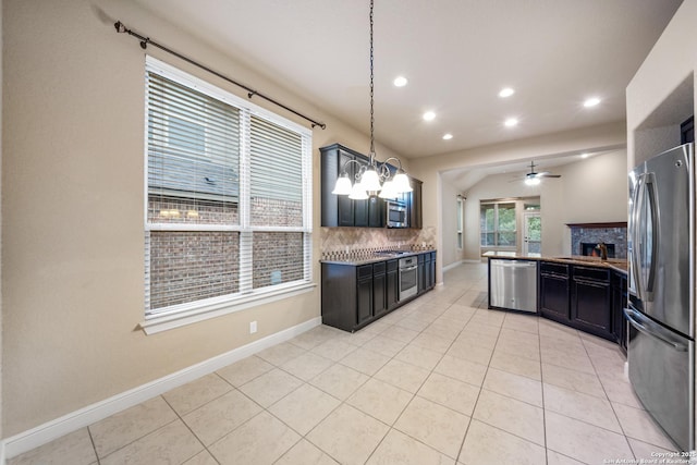 kitchen featuring a stone fireplace, hanging light fixtures, light tile patterned floors, stainless steel appliances, and decorative backsplash