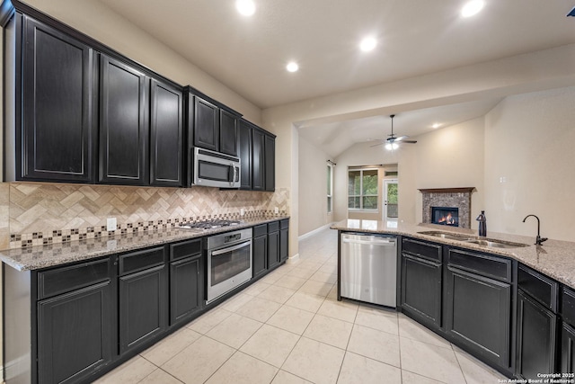 kitchen featuring a fireplace, sink, decorative backsplash, light stone counters, and stainless steel appliances