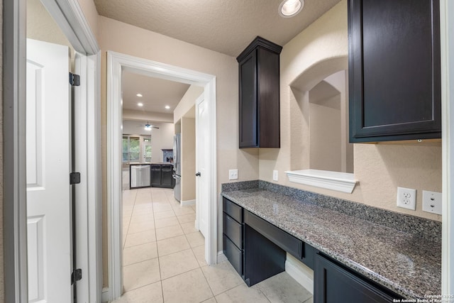 kitchen with light tile patterned flooring, appliances with stainless steel finishes, dark stone countertops, and a textured ceiling