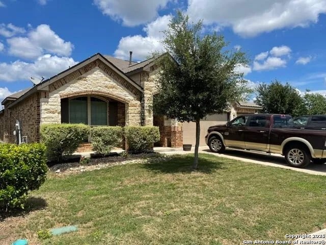 view of property hidden behind natural elements with stone siding, a garage, and a front yard