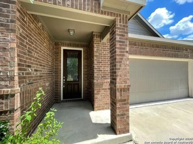 view of exterior entry featuring a garage, brick siding, and driveway