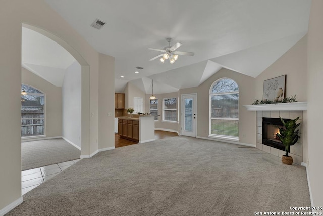 unfurnished living room with lofted ceiling, visible vents, a ceiling fan, light carpet, and a tile fireplace