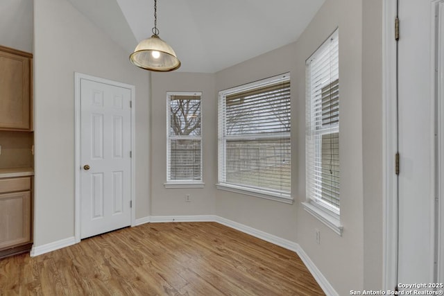 unfurnished dining area featuring light wood-type flooring, baseboards, and vaulted ceiling