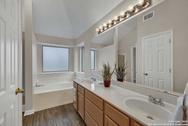 full bathroom featuring lofted ceiling, a garden tub, a sink, and double vanity