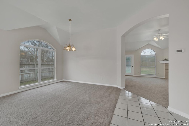 empty room featuring light tile patterned floors, ceiling fan with notable chandelier, vaulted ceiling, and light colored carpet