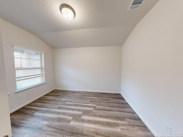 empty room with lofted ceiling, a textured ceiling, and light wood-type flooring