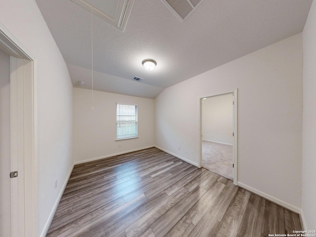 empty room featuring lofted ceiling, hardwood / wood-style floors, and a textured ceiling