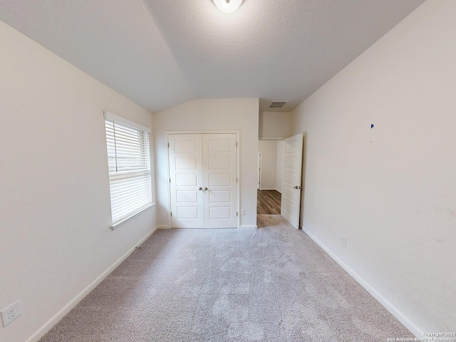 unfurnished bedroom with a closet, vaulted ceiling, light carpet, and a textured ceiling