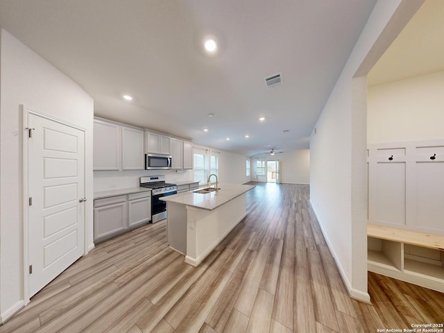 kitchen with stainless steel appliances, sink, a kitchen island with sink, and light hardwood / wood-style flooring