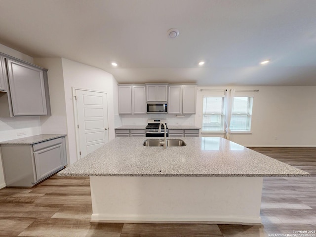 kitchen featuring appliances with stainless steel finishes, sink, a center island with sink, and gray cabinetry