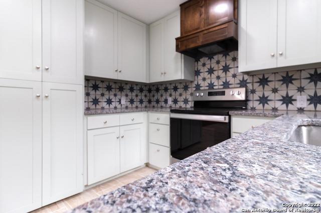 kitchen featuring stainless steel range with electric stovetop, light stone countertops, custom range hood, white cabinets, and decorative backsplash