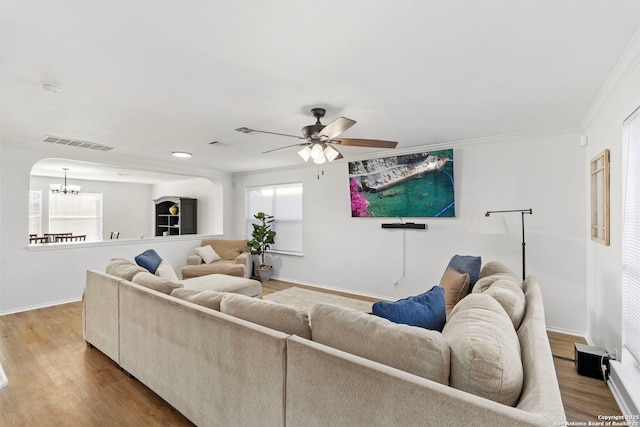 living room featuring wood-type flooring, plenty of natural light, ceiling fan with notable chandelier, and crown molding