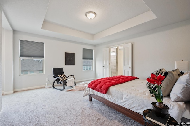 carpeted bedroom featuring a raised ceiling and baseboards