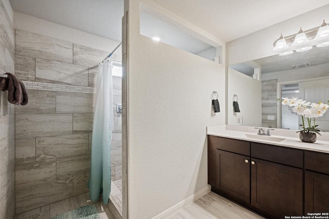 full bathroom featuring visible vents, a tile shower, vanity, wood finished floors, and baseboards