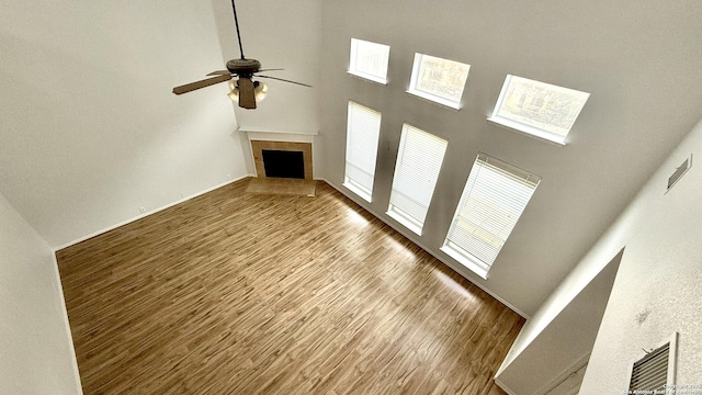 unfurnished living room featuring ceiling fan, wood-type flooring, a tiled fireplace, and a towering ceiling