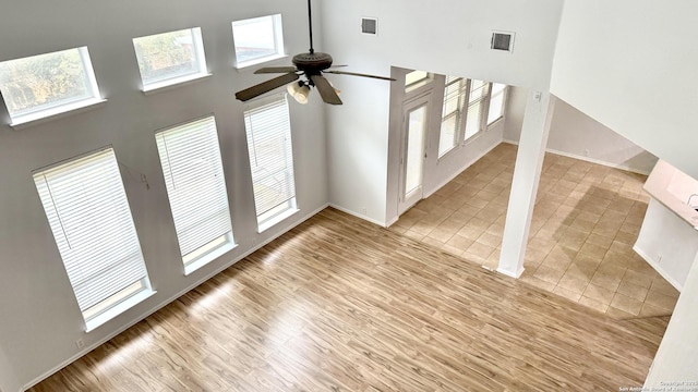 unfurnished living room with ceiling fan, a towering ceiling, and light hardwood / wood-style flooring