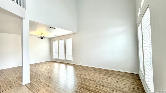 unfurnished room featuring an inviting chandelier, a towering ceiling, and light wood-type flooring