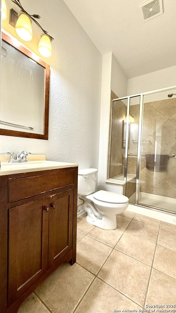 bathroom with tile patterned floors, vanity, toilet, and a shower with shower door