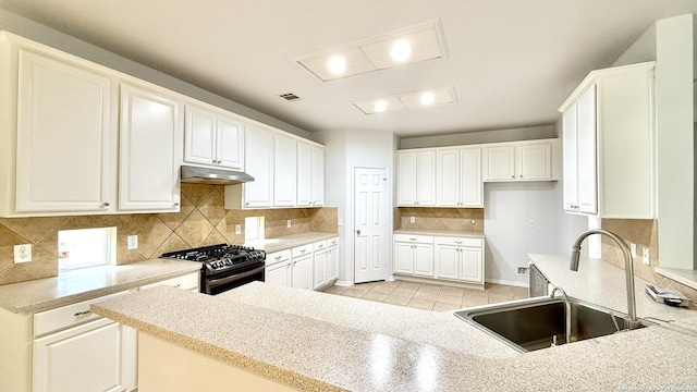 kitchen featuring sink, stainless steel gas range, backsplash, white cabinets, and kitchen peninsula