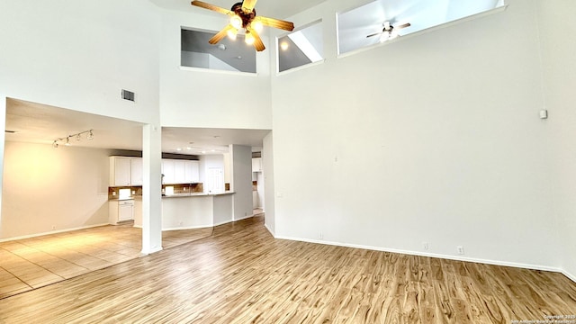 unfurnished living room with rail lighting, light wood-type flooring, and ceiling fan