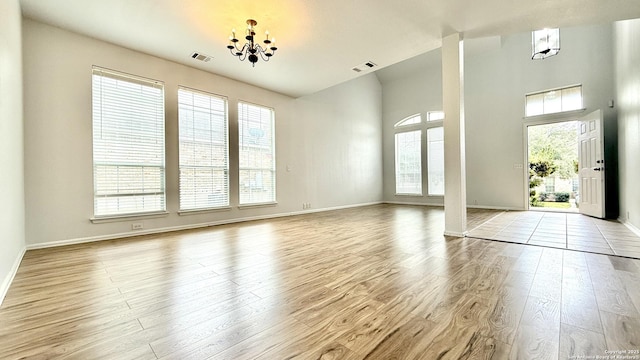 interior space featuring a towering ceiling, a healthy amount of sunlight, light hardwood / wood-style floors, and a notable chandelier