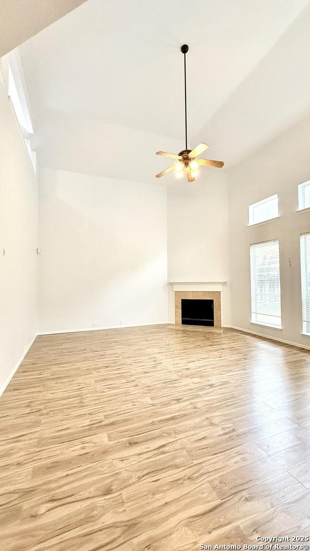 unfurnished living room with a tiled fireplace, ceiling fan, high vaulted ceiling, and light wood-type flooring