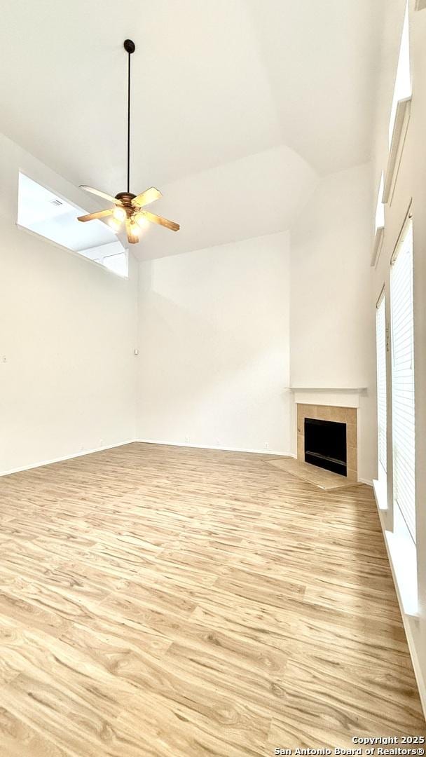 unfurnished living room featuring ceiling fan, high vaulted ceiling, a fireplace, and light hardwood / wood-style floors