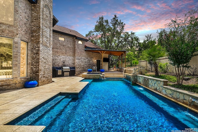 pool at dusk with a patio, pool water feature, a grill, and exterior kitchen