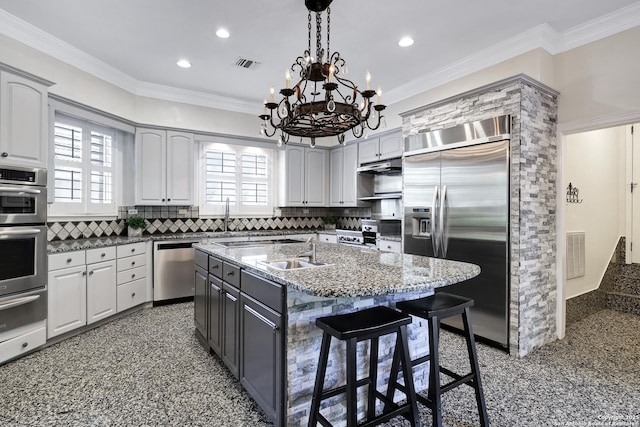 kitchen featuring sink, a breakfast bar area, a kitchen island with sink, stainless steel appliances, and light stone countertops