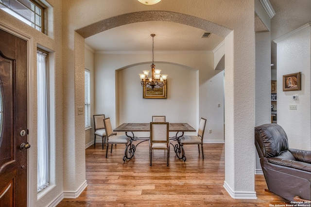 dining space with an inviting chandelier, crown molding, light hardwood / wood-style flooring, and a wealth of natural light