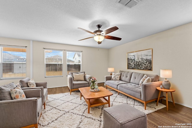 living room with ceiling fan, a textured ceiling, and light wood-type flooring