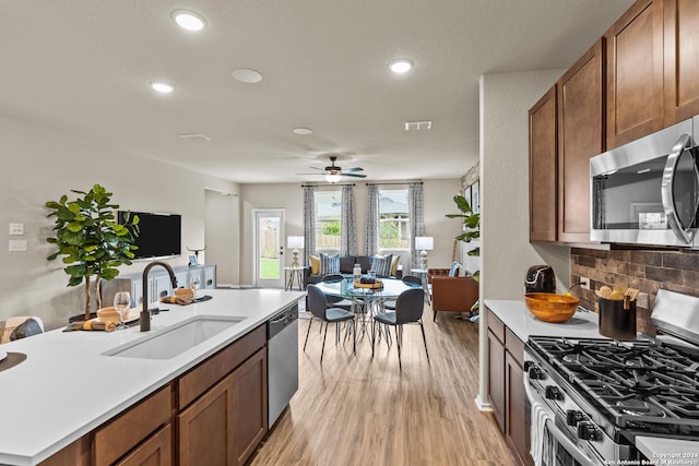 kitchen featuring sink, ceiling fan, backsplash, stainless steel appliances, and light wood-type flooring